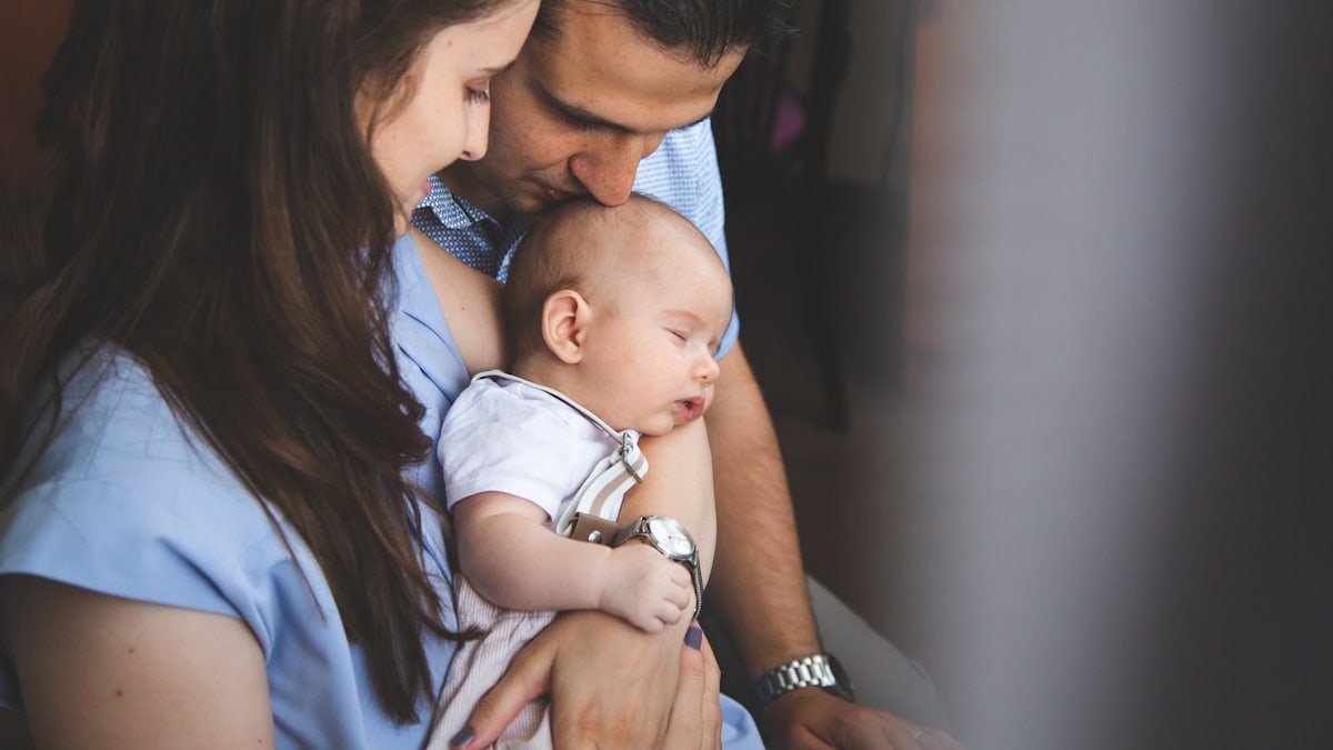 Parents holding their young baby boy, him sleeping.